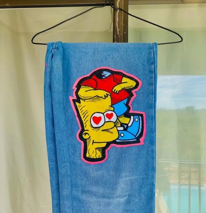 Hand-painted cartoon character with heart eyes on light-wash denim hanging on a hanger