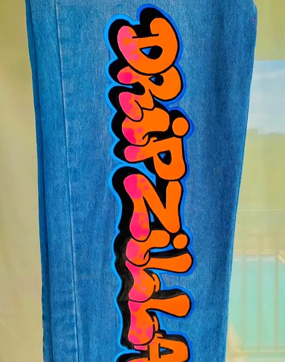 Orange and pink bubble lettering hand-painted down the leg of blue denim jeans