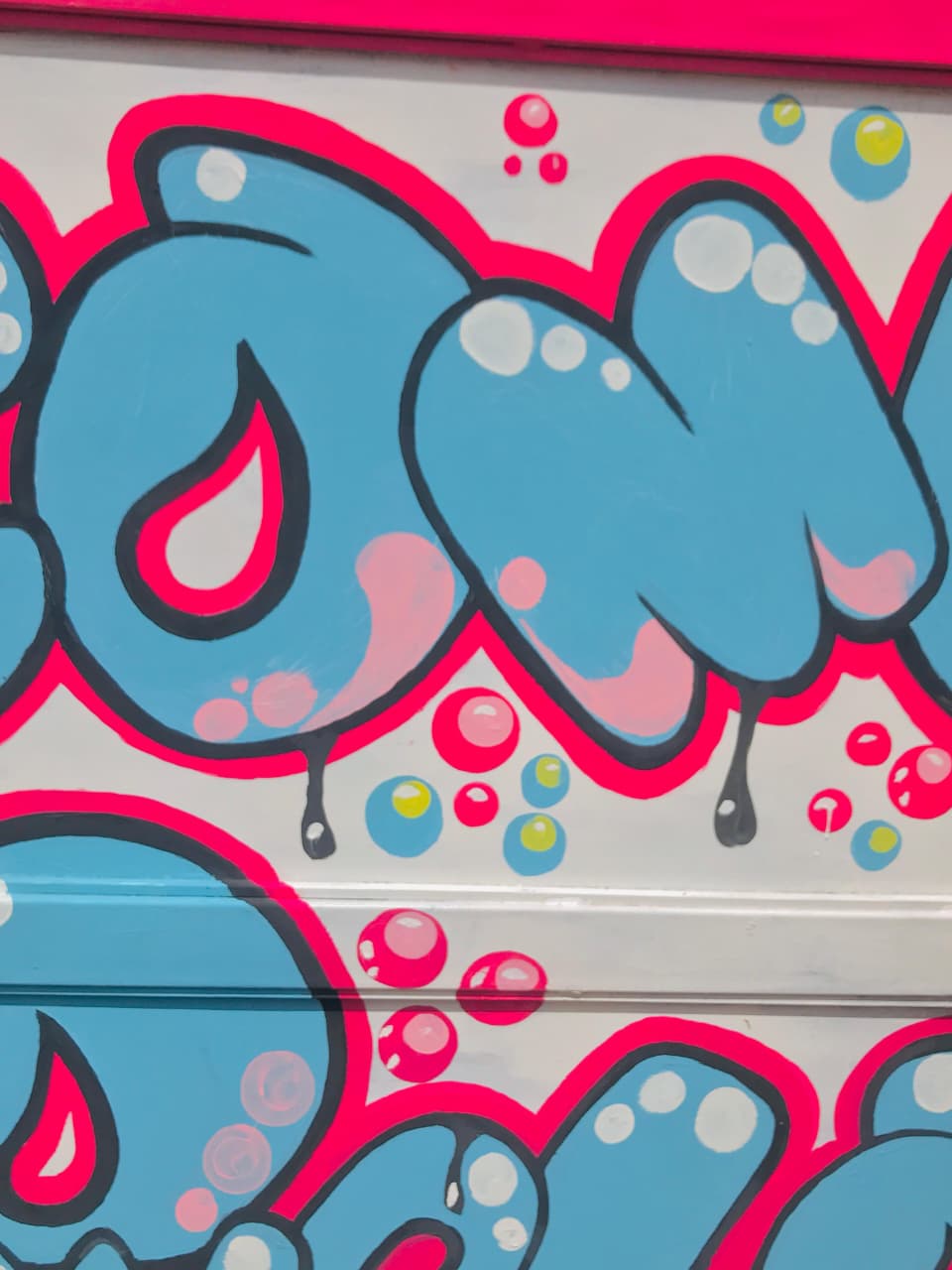 Close-up of a mural with blue bubble letters, pink outlines, paint drips and floating bubbles