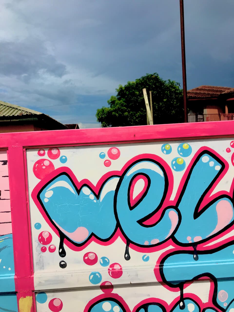Painted welcome mural in front of houses under a stormy sky