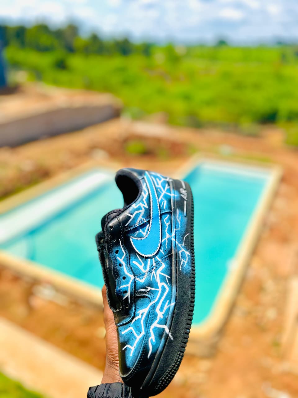 Side view of a hand-painted lightning sneaker held above a swimming pool